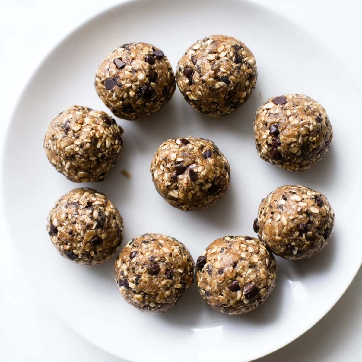 Bite-sized no bake chocolate peanut butter protein balls studded with mini dark chocolate chips on a white plate