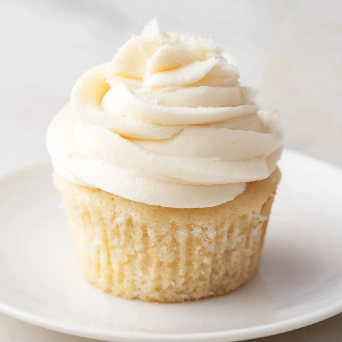 Fluffy vanilla cupcakes topped with creamy buttercream frosting on a white plate