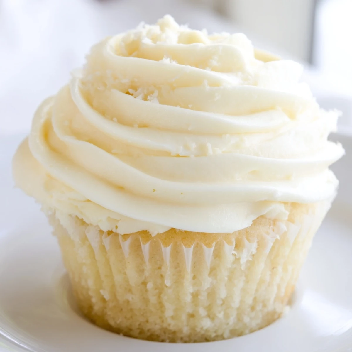 Light golden vanilla cupcakes piped with swirled white frosting and colorful sprinkles