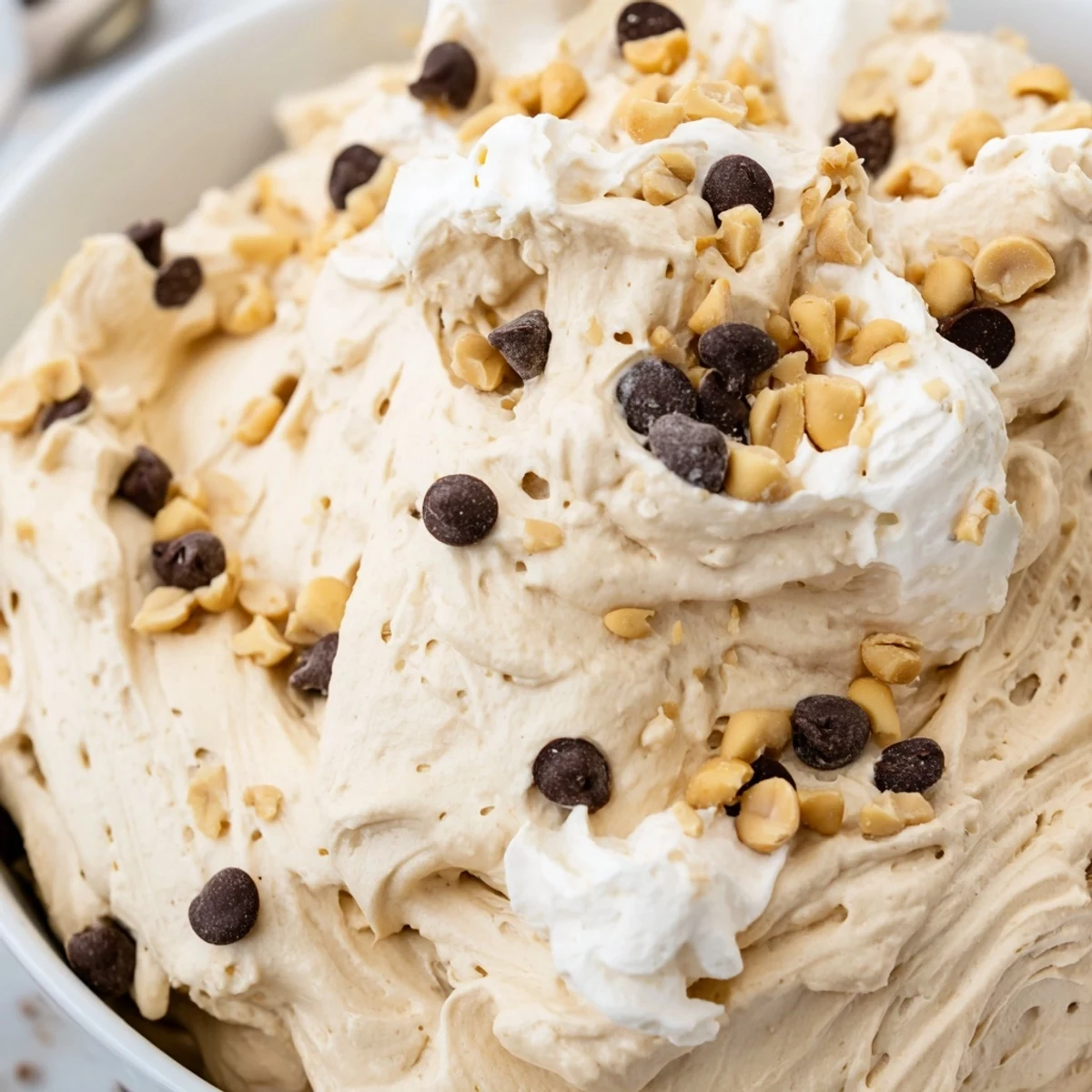 Creamy peanut butter and Cool Whip mousse topped with chopped roasted peanuts and mini chocolate chips in a clear glass