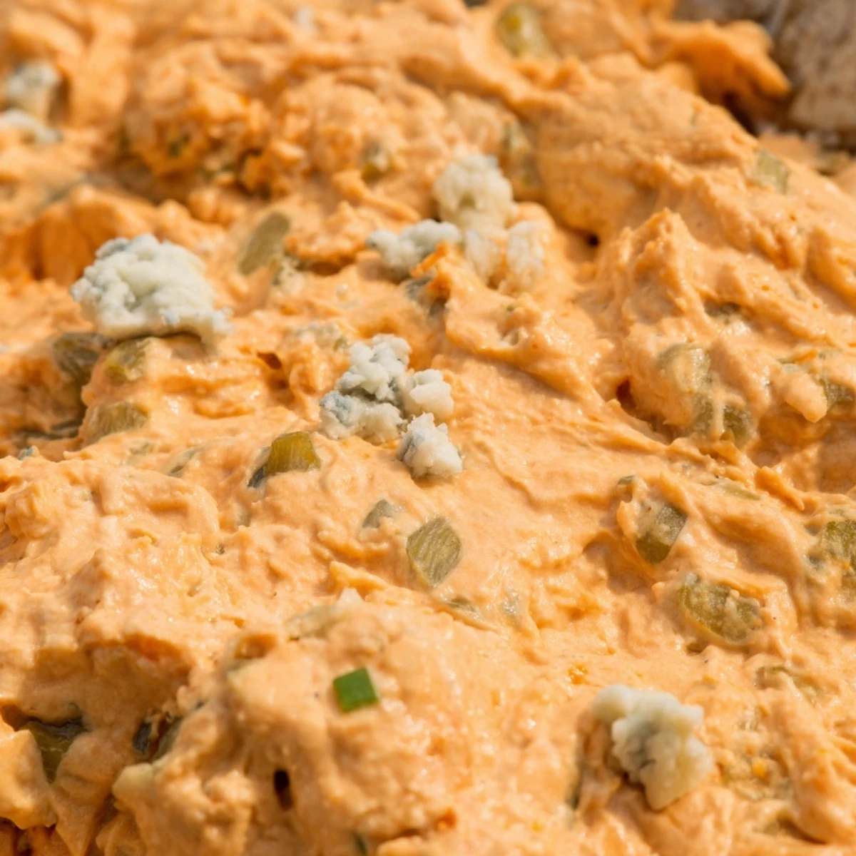 Creamy buffalo pickle dip in a serving bowl surrounded by crispy chips and fresh veggie sticks