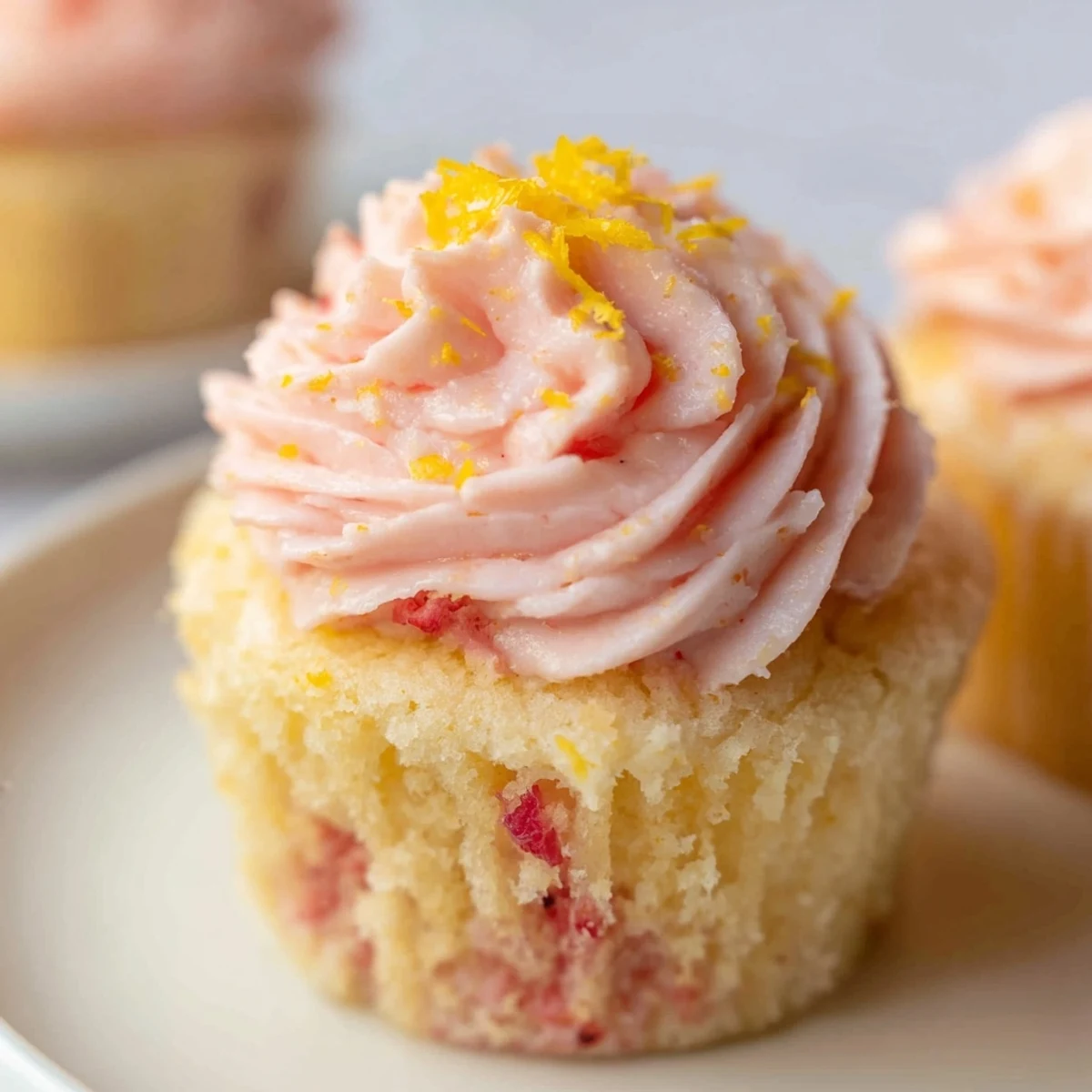 Fresh strawberry lemonade cupcakes with fluffy pink frosting piped high and garnished with lemon zest