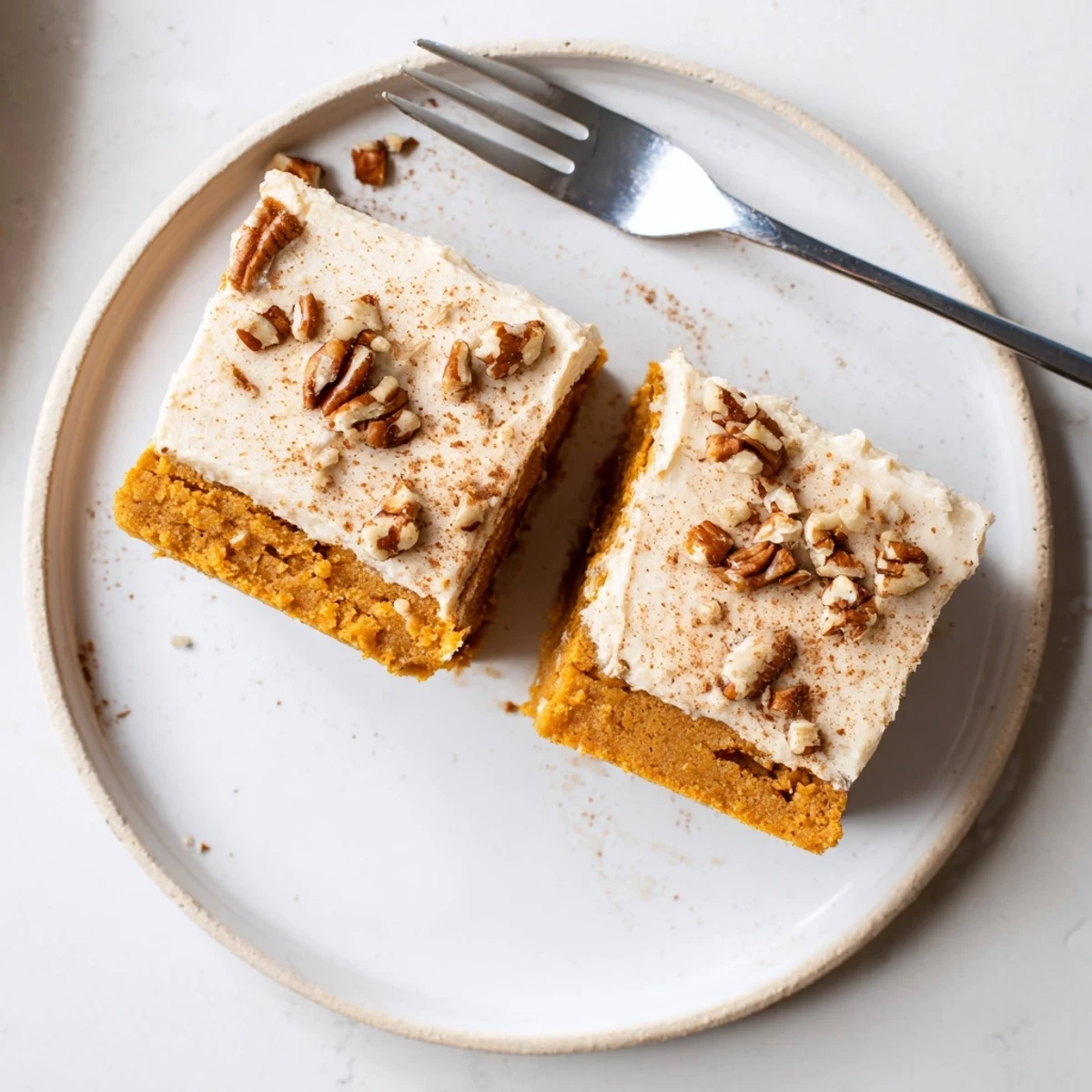 Warm spiced pumpkin bars with cream cheese frosting sliced and arranged on a rustic baking sheet