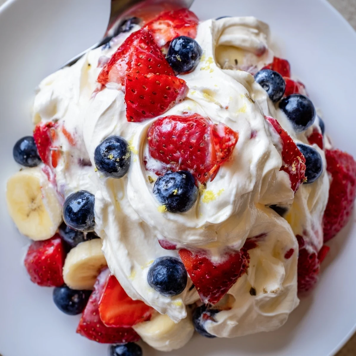 A bowl of Red White And Blue Cheesecake Salad topped with sliced bananas