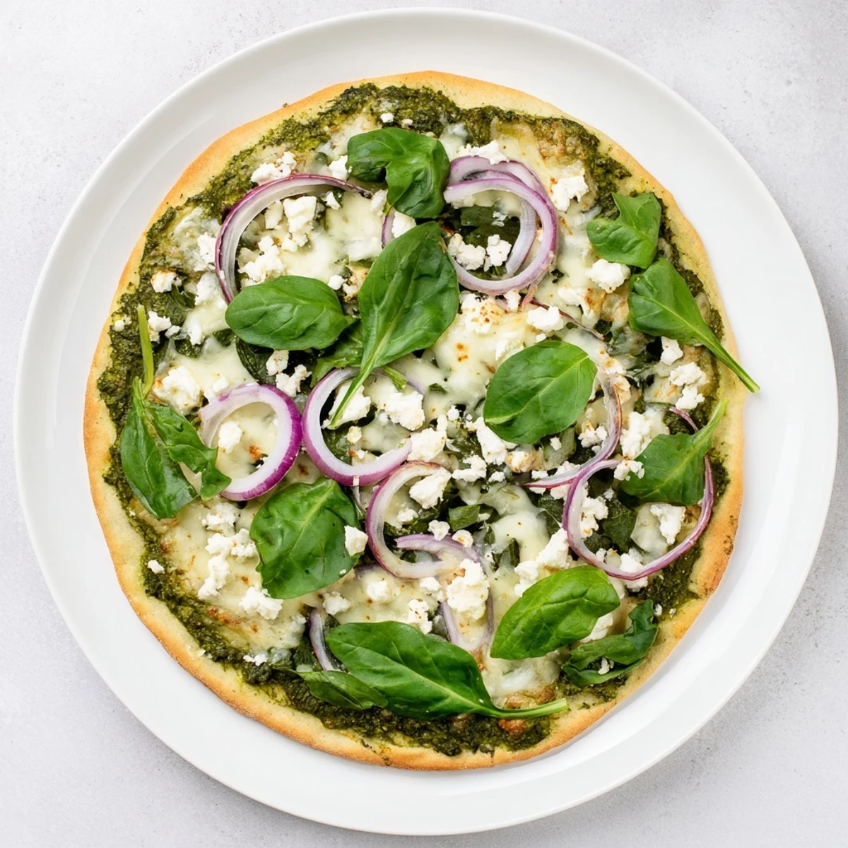 Sliced green pizza featuring zesty broccoli pesto base with arugula, red onion, and creamy feta
