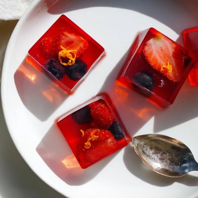 Homemade collagen fruit jellies topped with fresh berries in colorful silicone molds